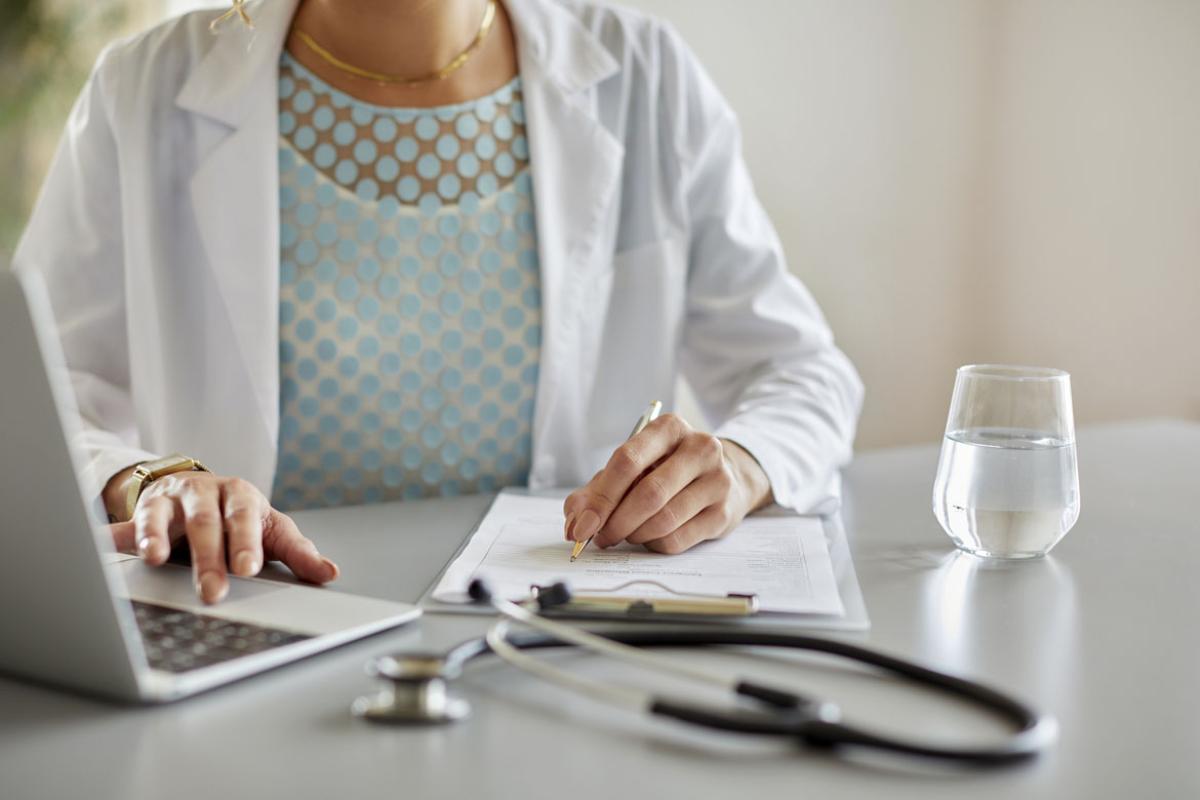 Doctor doing paperwork while using laptop