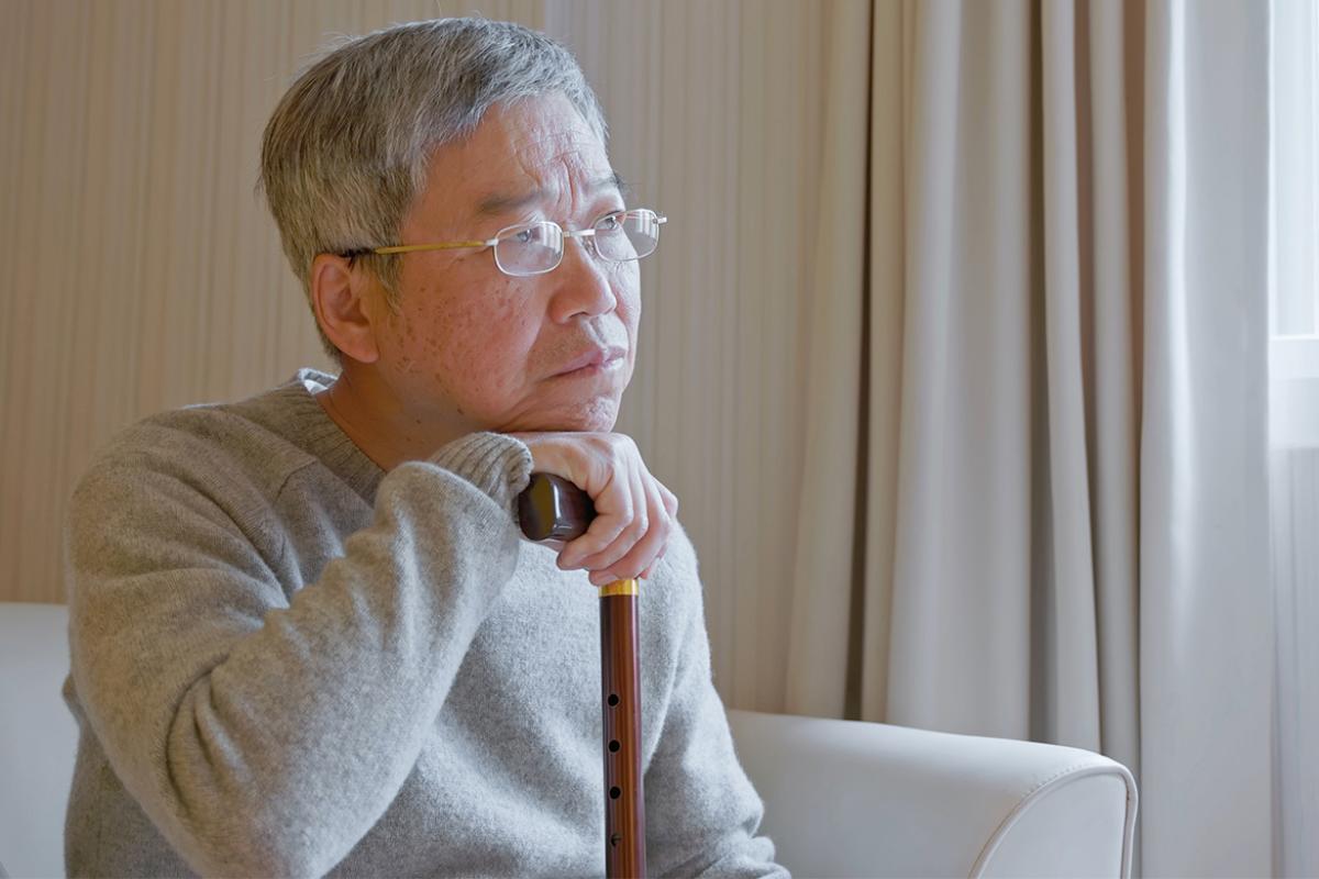 Solemn person rests chin on cane