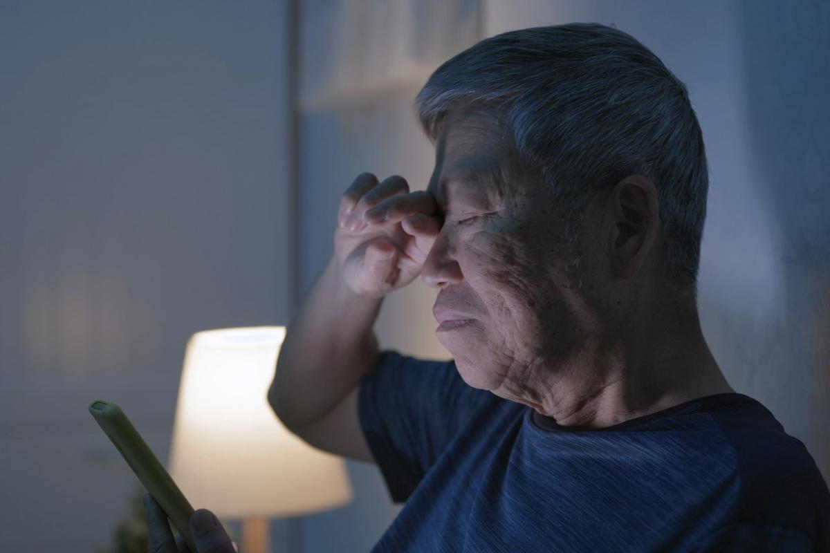 Tired man scrolls through a smartphone in a darkened bedroom
