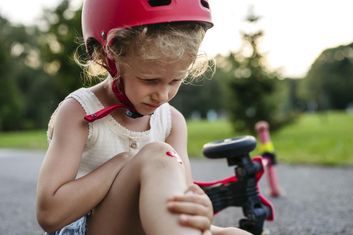 Sad young child tending to an injury after a fall from a bike