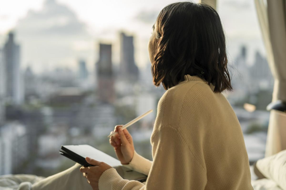 Young adult holds a digital table while looking out a window