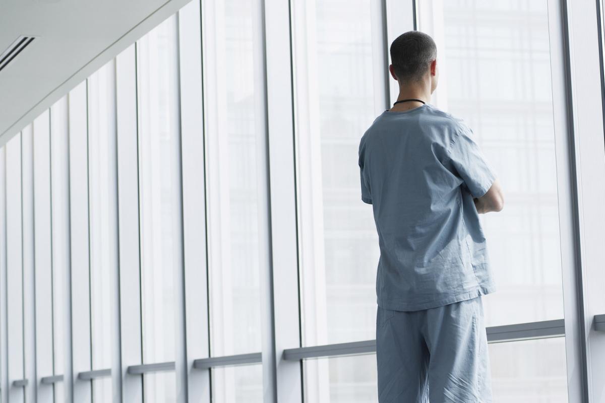 Healthcare worker looks out window of hospital corridor
