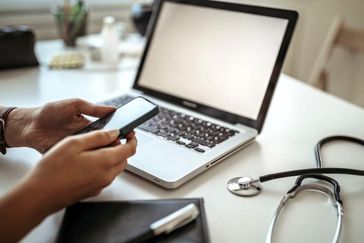 Physician holds a smartphone in front of a laptop