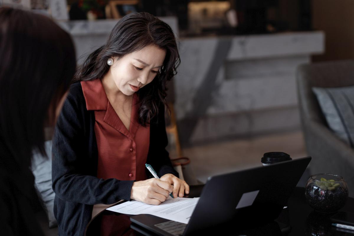 Businessperson signs documents while collaborating with a colleague