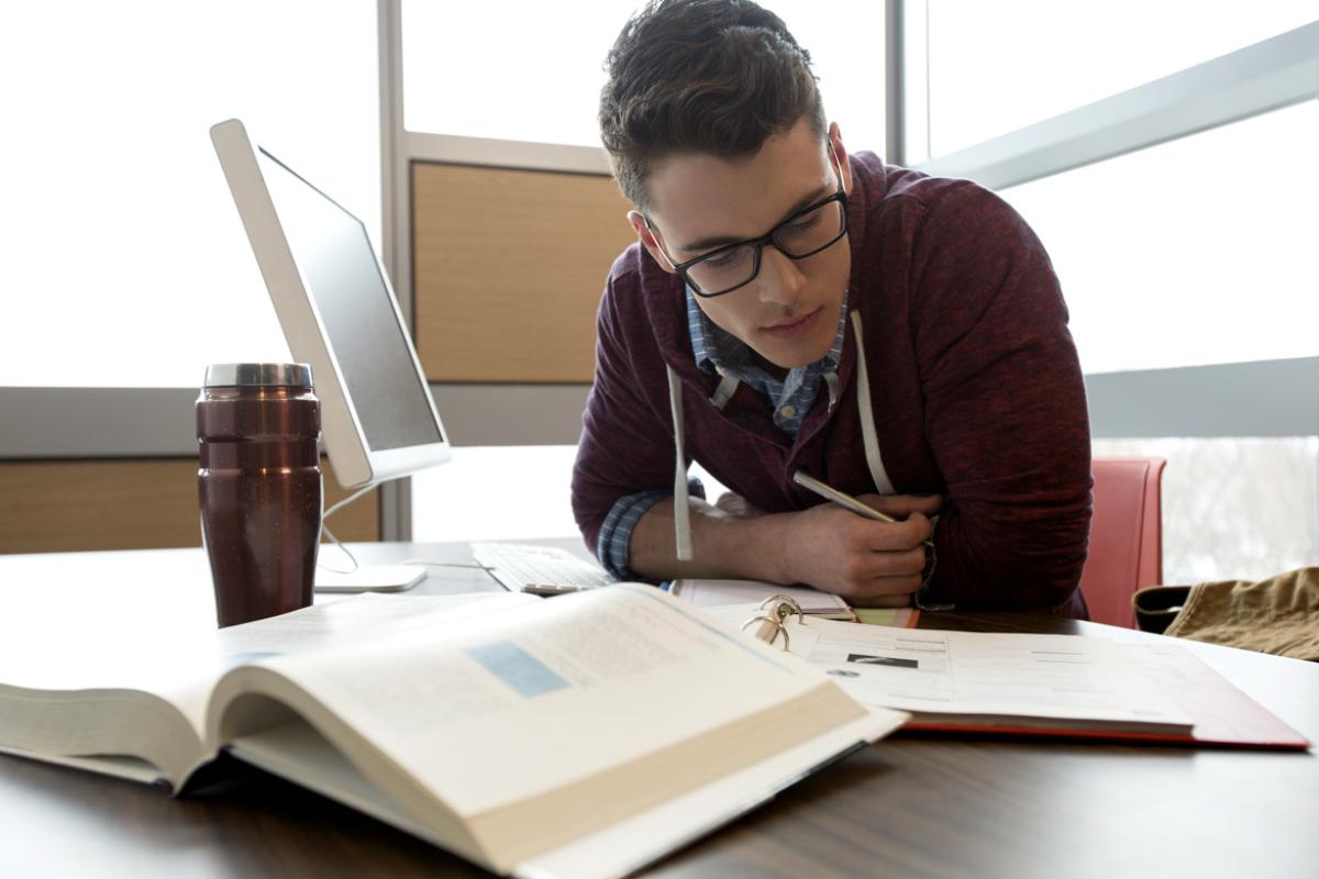 A medical student sits near a laptop and studies his books before an exam.