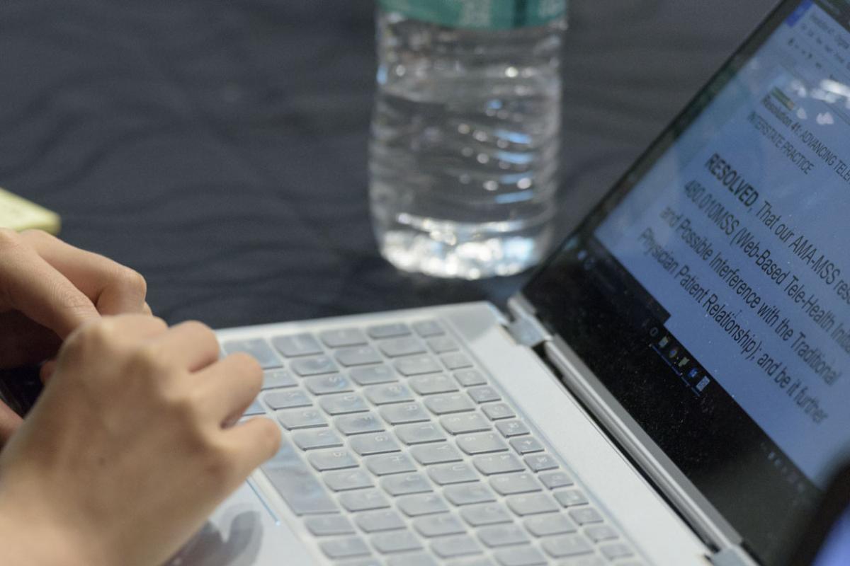 Hands writing a paper on a laptop.