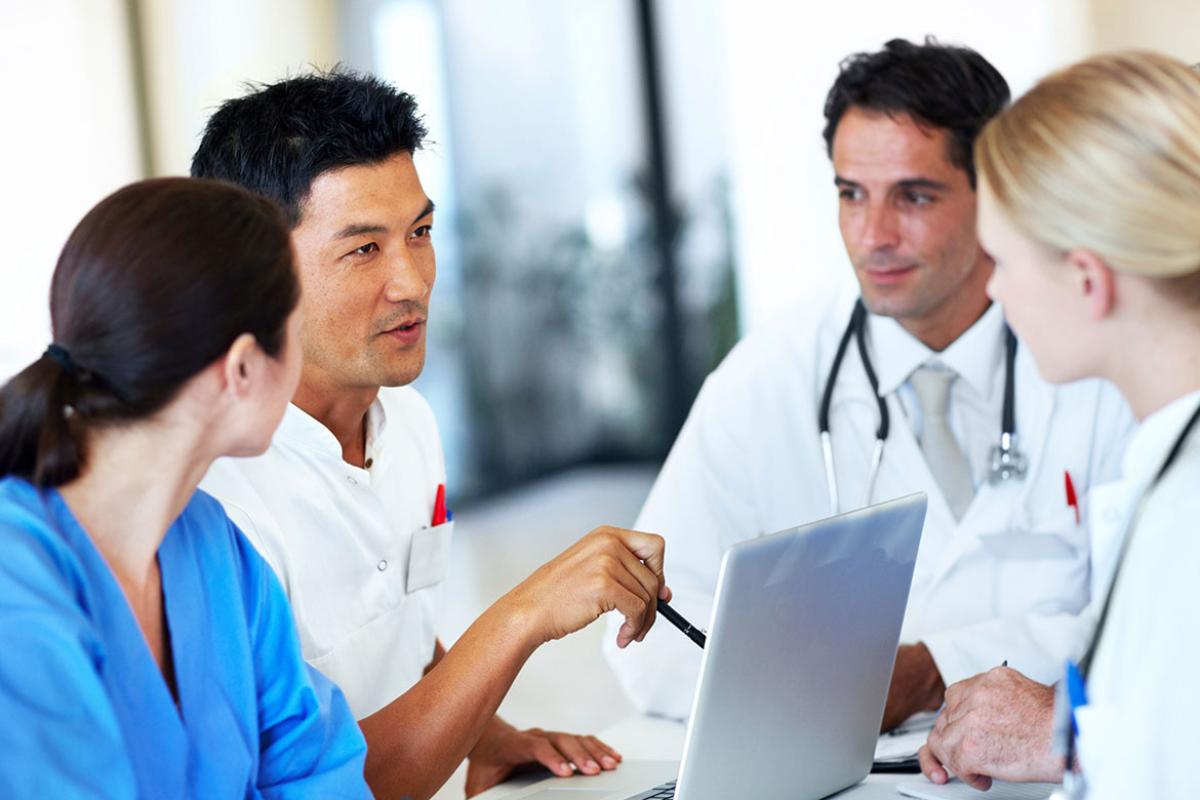 Four physicians have discussion around a laptop.