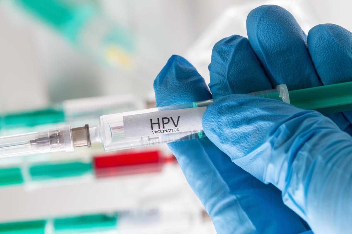 Hand in surgical glove holds HPV vaccine.