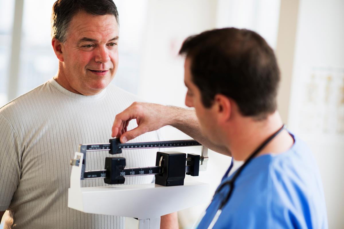 Physician weighing male patient on scale.