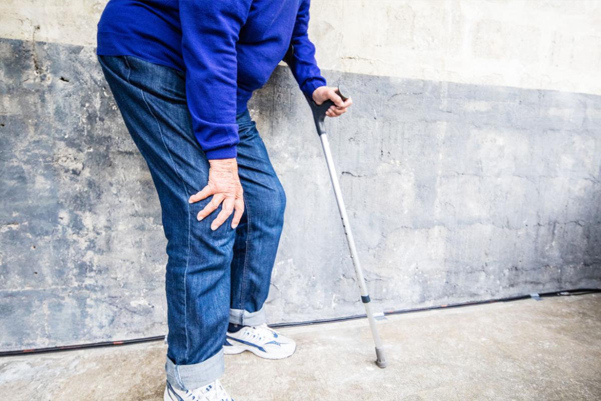 Man in chronic pain holds cane and his sore knee.