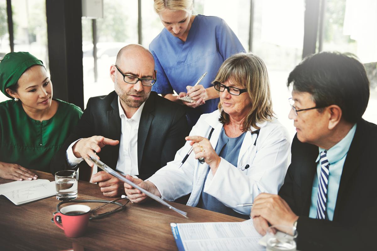 Five physicians around a table working from a tablet.