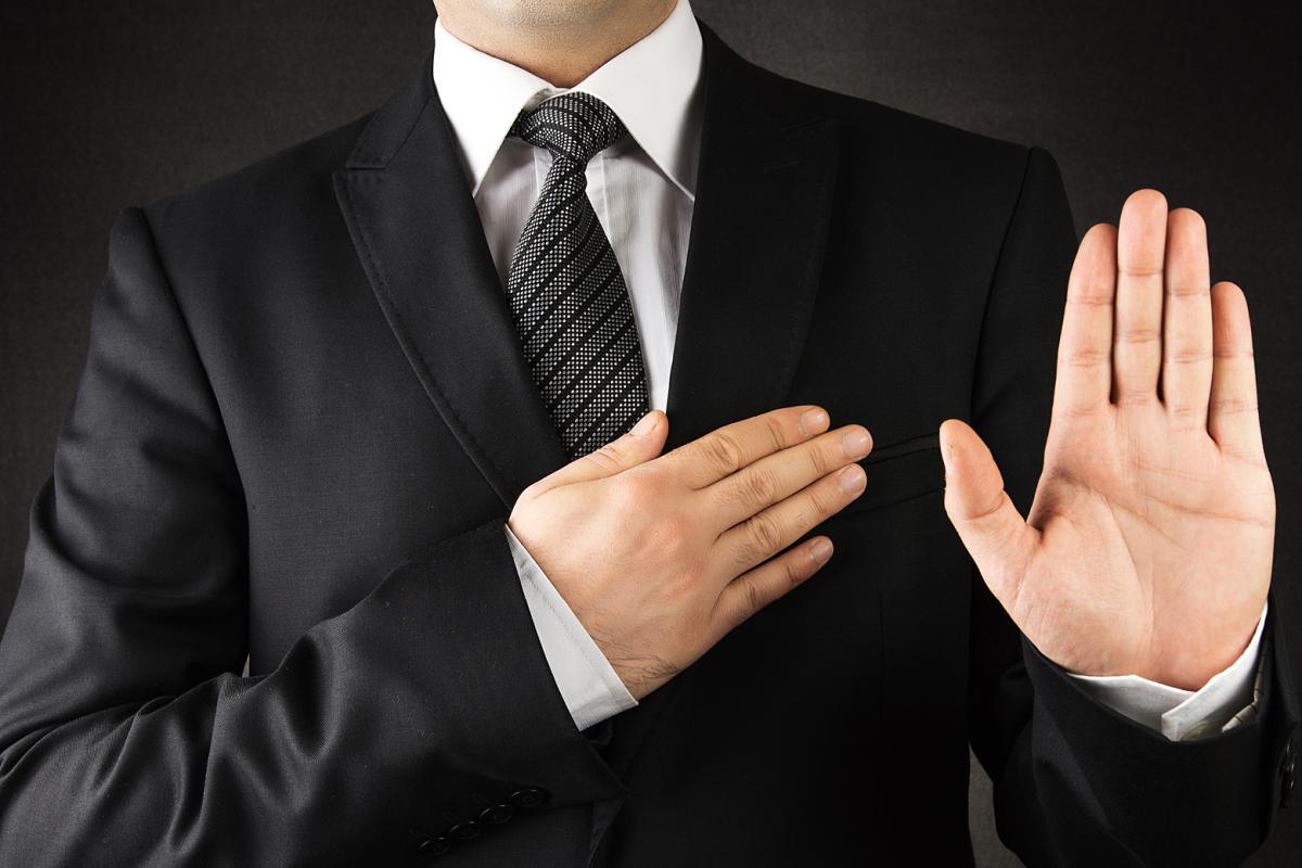 Man with one hand over his heart, holding up his other hand taking an oath. 
