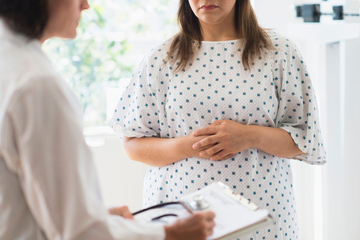 Physician takes notes as patient holds her midsection. 