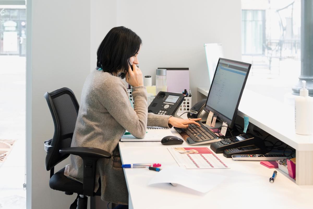 Clinic worker answers phone while working on computer.