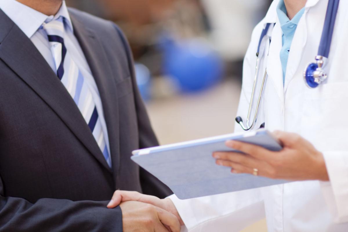 Man in suit shakes hand of physician holding tablet