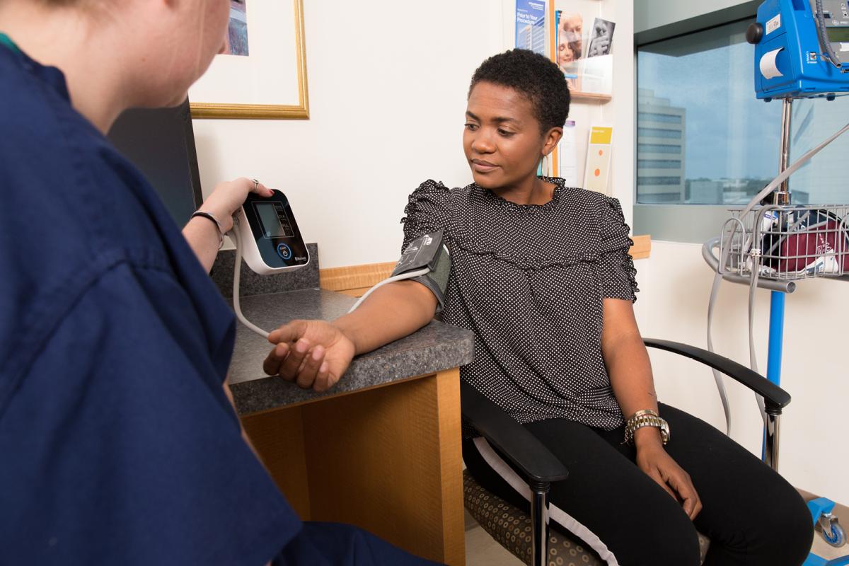 An African-American woman gets her blood pressure taken while a nurse watches.