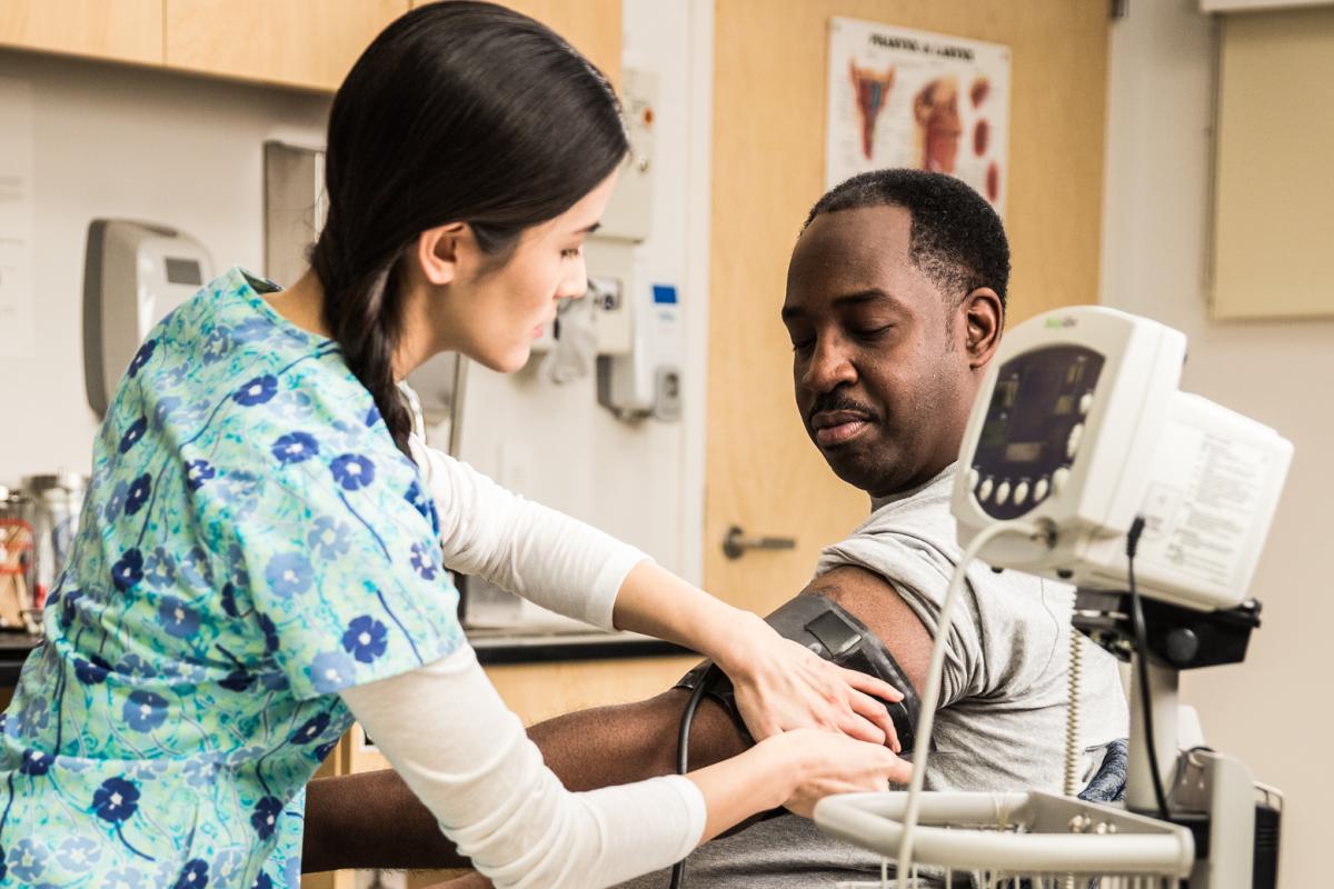 A female nurse administers a blood pressure test to an African-American man. 