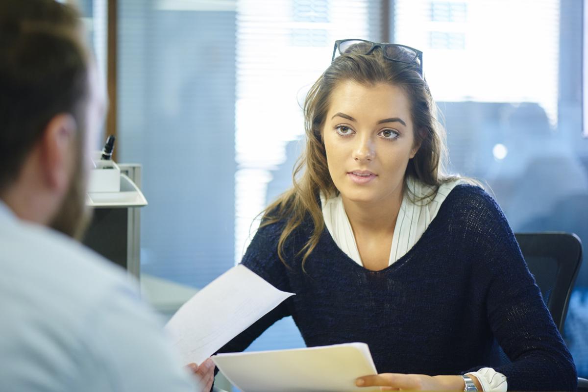 A woman reviewing papers while having a conversation with a man.