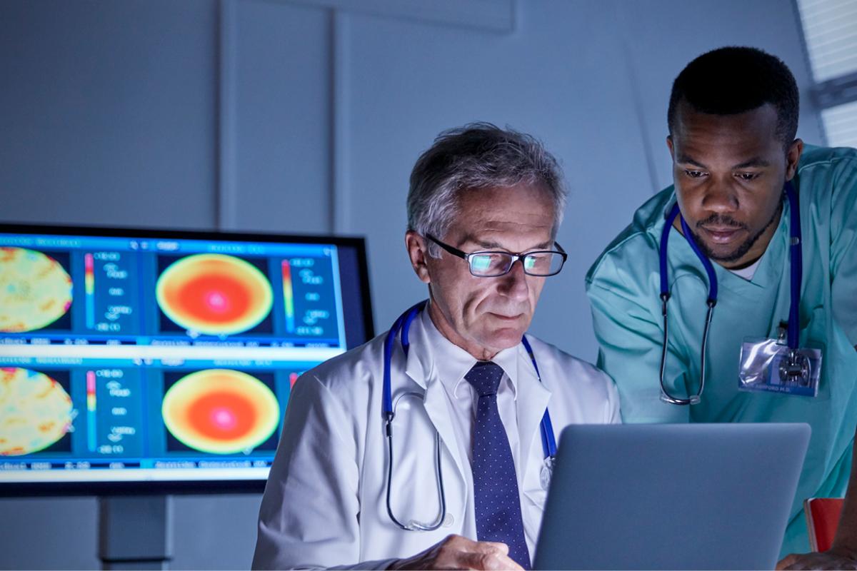 A diverse group of doctors reviewing a laptop with medical readouts in the background.